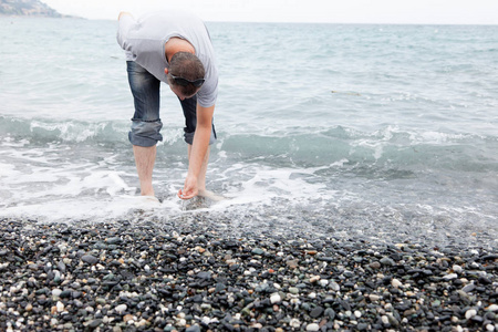 在岩石海滩上收集鹅卵石的人