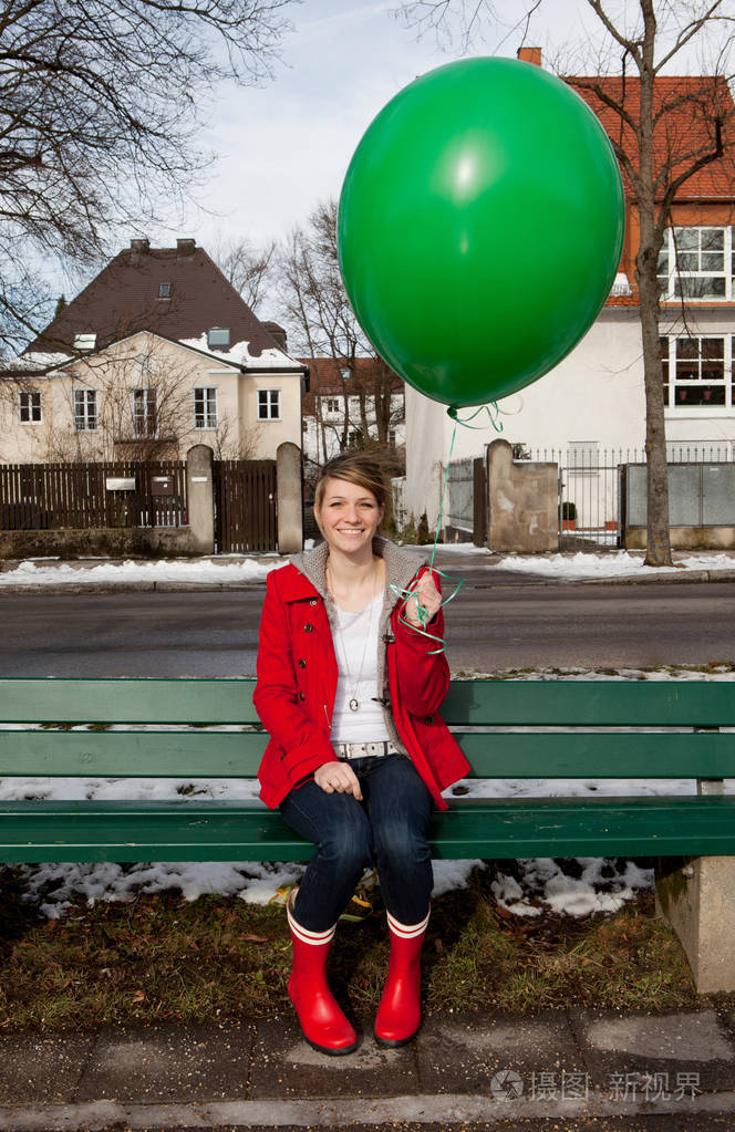 美丽的年轻白种人女人坐在长凳上拿着绿色的气球
