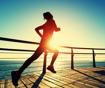 运动的年轻女子日出时在海滨木板路上跑步照片