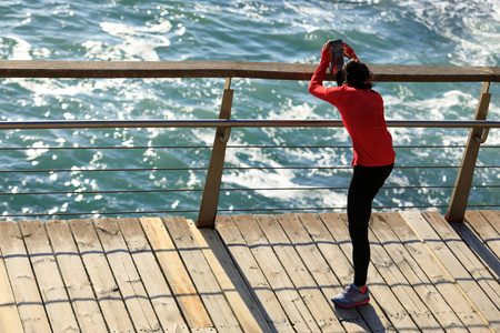 运动的年轻女子在海滨木板路上伸腿