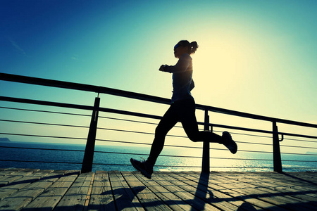 运动的年轻女子日出时在海滨木板路上跑步照片