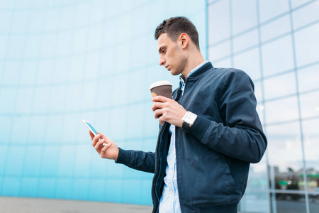 一个拿着纸杯咖啡的男人穿过城市,一个穿着时髦衣服的帅哥,手里拿着