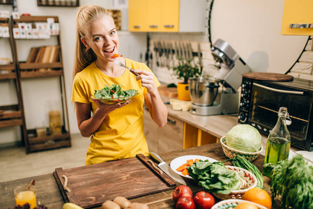 快乐的女人在厨房里吃沙拉，健康的生物食品烹饪。 素食