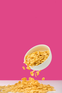近距离观看白色碗，玉米片倒在粉红色上