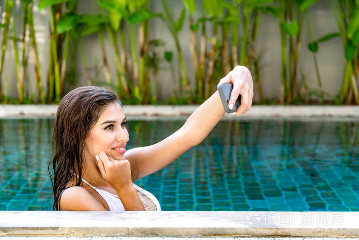 游泳池里美丽的年轻单身白人女人使用手机自拍穿白色比基尼连接的世界