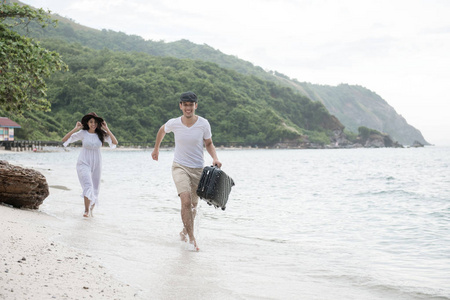 一对夫妇在海滩上跑步。 年轻快乐的跨种族夫妇在海滩上奔跑和追逐。 亚洲女人高加索男人。 年轻的混合种族浪漫概念。