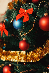用彩色的红色蓝色的球金色的金属箔红色的蝴蝶结金色的珠串闪光的和温暖的灯光细节来装饰圣诞树。新年和假日2018概念