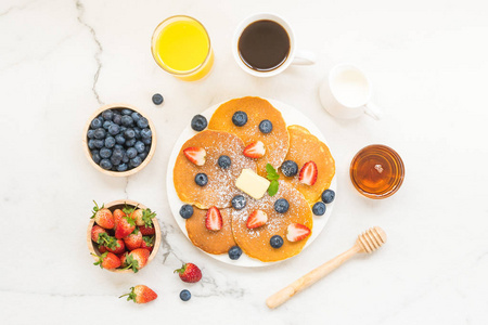 健康早餐，包括煎饼蓝莓和草莓水果黑咖啡牛奶和橙汁，背景为白石桌