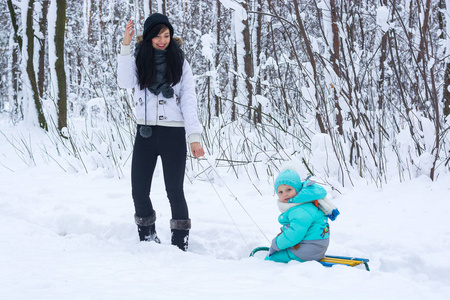 年轻的妈妈带着她的孩子在冬天公园的雪橇上