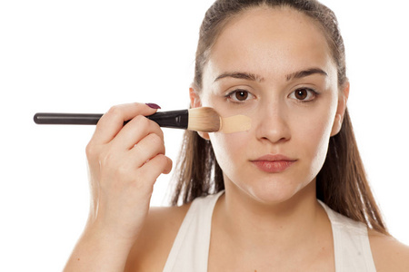 年轻女子用刷子在脸上涂上液体粉底照片