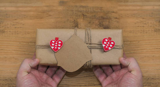 礼品盒绳子上的夹子上有两颗红色的心，用棕色的工艺纸包裹。