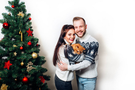 愉快的家庭夫妇在毛衣与猫在白色背景的圣诞树附近