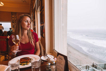 女孩坐在窗边，在旧金山的悬崖屋餐厅看到海景。