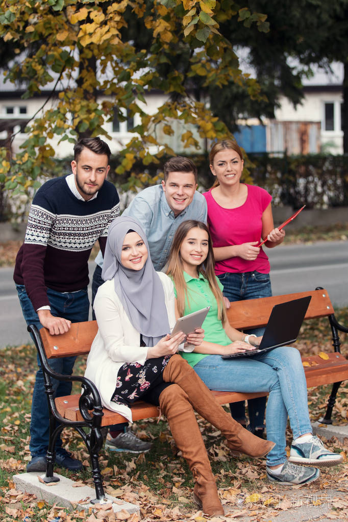 年轻人在公园的长椅上使用笔记本电脑和平板电脑玩得很开心在外面聊天