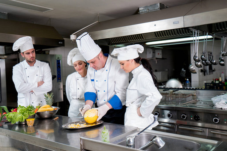 厨房厨师和年轻学徒一起教学,制作装饰水果篮照片