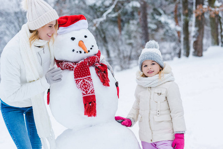 美丽快乐的母女和雪人站在冬天的公园里