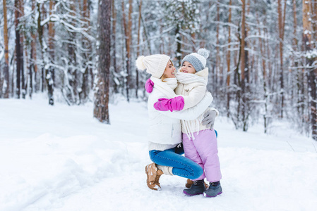 微笑的女儿和母亲在冬天的森林里拥抱在一起