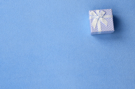 一个蓝色的小礼品盒，有一个小蝴蝶结，躺在柔软而毛茸茸的浅蓝色羊毛织物的毯子上。 打包礼物送给你可爱的女朋友