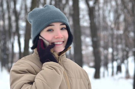冬天公园里漂亮迷人的高加索穿洞女孩的肖像。 她在用现代智能手机说话。 青年街头时尚。 冬天的乐趣。 在露天散步。