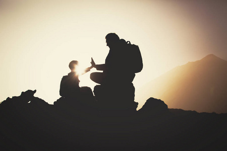 父亲和儿子的剪影在山上徒步旅行在日落