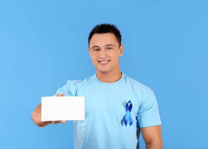年轻男子在 tshirt 与蓝丝带持有空白卡的颜色背景。前列腺癌认知概念