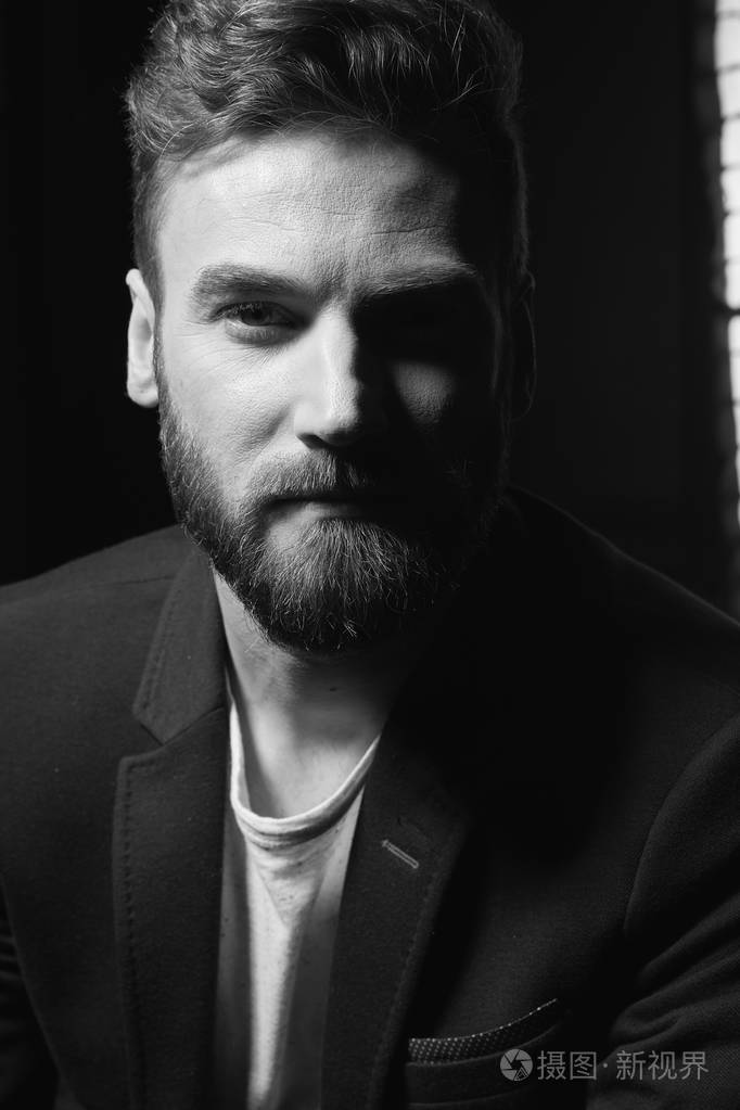 黑白特写照片年轻迷人的男人留着深色头发胡子戴着深色夹克摄影棚