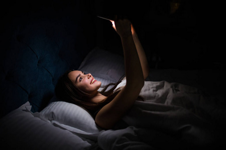 睡觉黑夜在黑夜睡觉前使用智能手机的年轻女性照片