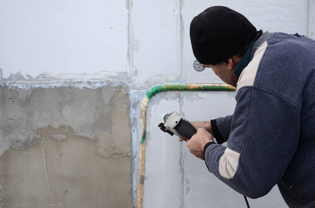 一位年长的工人在发泡胶墙上钻了一个洞，以便随后安装一个塑料加强销。 用钻头在墙上打洞。 建筑物立面的升温