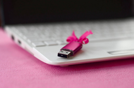 明亮的粉红色usb闪存卡与粉红色蝴蝶结躺在一条柔软和毛茸茸的浅粉红色羊毛织物毛毯旁边的白色笔记本电脑。经典女性记忆卡礼物设计