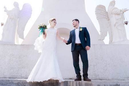 一个可爱的情侣蜜月的肖像在一个婚礼上的花束在手反对东正教纪念碑的背景与天使