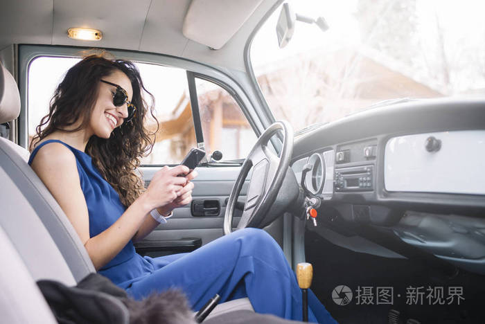 美丽的年轻女子在车里用她的手机