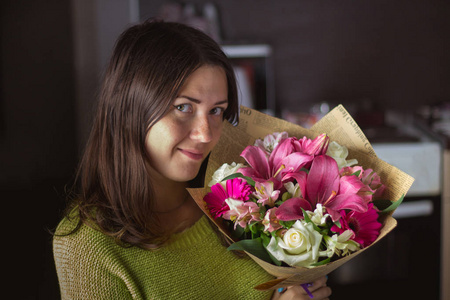 美丽的女孩与黑头发与一束鲜花从百合, 非洲菊, 白玫瑰和 alstroemeria 在一个黑暗的背景。节日, 礼物