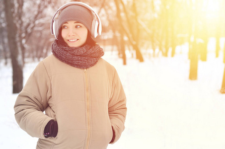 漂亮的年轻女孩戴着温暖的冬天耳罩和围巾。 有趣的黑发女性模特在寒冷的天气里带着耳机走在外面。 微笑快乐的模特摆姿势。 好天气
