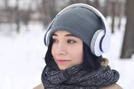 一幅美丽迷人的白种人穿洞女孩海普斯特冬季公园的肖像。她正在耳机上听音乐。年轻时尚。冬天的乐趣。