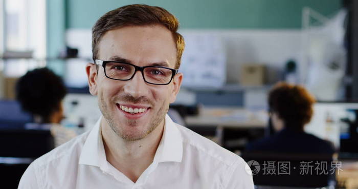 穿着白色衬衫的白种帅哥戴着眼镜直视着镜头乐呵呵地微笑着模糊的办公