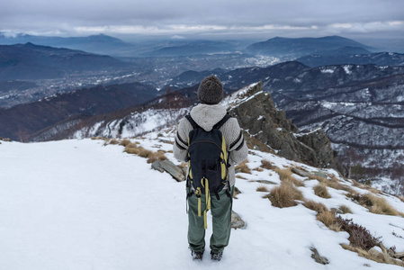 女背包徒步旅行者在阿尔卑斯山的高处看风景。后视, 冬冷雪, 乌云密布