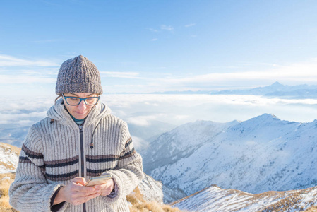 在山上使用智能手机的妇女。白雪皑皑阿尔卑斯山的全景图在寒冷的冬季。用新技术共享生命时刻的概念