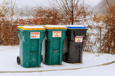 绿色的垃圾容器，一个收集塑料的容器，覆盖着白色蓬松的雪。 秋天的第一场雪。 垃圾容器雪冬天