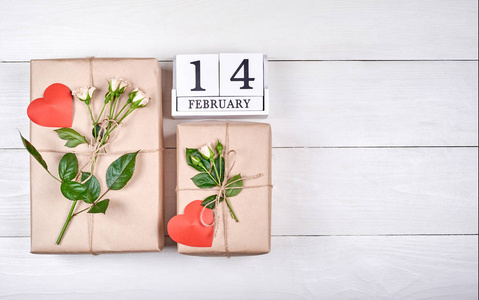 从2月14日的街区日历的顶部可以看到，礼品盒用牛皮纸包裹着新鲜的玫瑰和木制桌子上的红心，复制空间。出售，购物。情人节贺卡，平卧