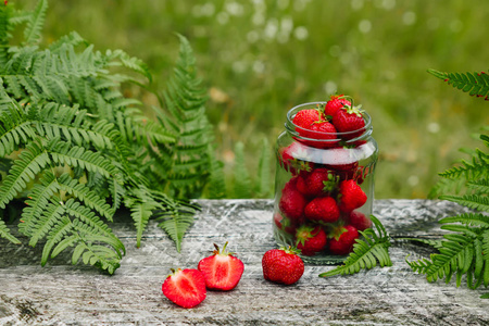 草莓放在玻璃罐里，放在木制的灰色桌子上，放在帕帕拉特尼克草莓季节的绿色背景叶子上。 opy文本空间
