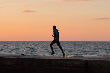 早上日出时，年轻的雄性跑步者在海洋或海滩上。