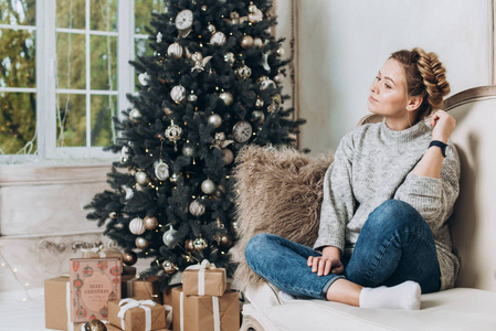 美丽的女孩坐在圣诞树附近，带着礼品盒。 圣诞节和新年的概念。 复制空间