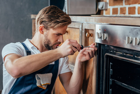 英俊的年轻修理工用螺丝刀修理烤箱