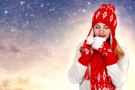美丽的年轻女子戴着一顶漂亮的针织帽子手套和围巾，喝着一杯茶。时尚的针织服装。圣诞快乐