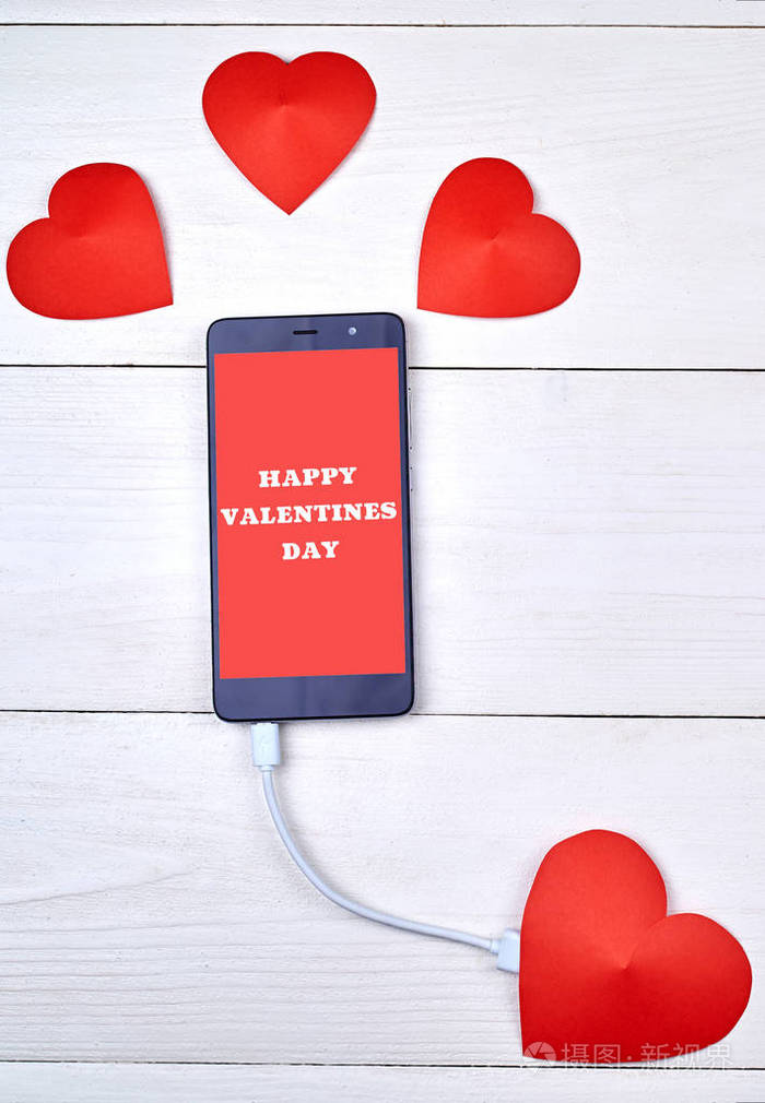 手机智能手机与标志快乐情人节充电与红色纸心在白色木制背景,复制