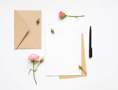 白色背景上的文字和生态纸信封。邀请卡或用粉红玫瑰的情书。顶视图，平躺假日概念