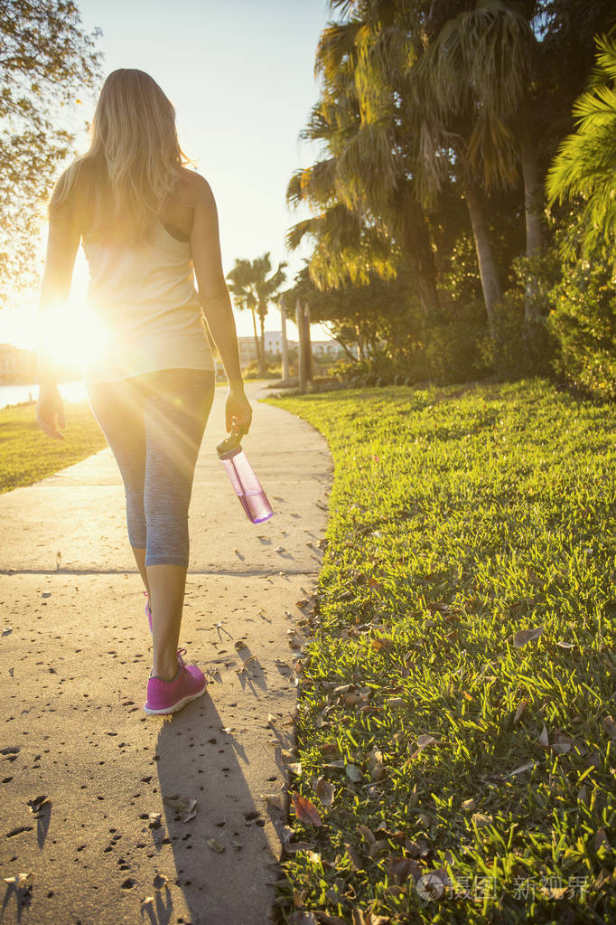 一个阳光明媚的夜晚美丽的金发女性慢跑者沿着城市公园