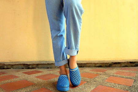 蓝色拖鞋时尚。 女人穿蓝色凉鞋和蓝色牛仔裤站在瓷砖地板背景上，非常适合任何用途。