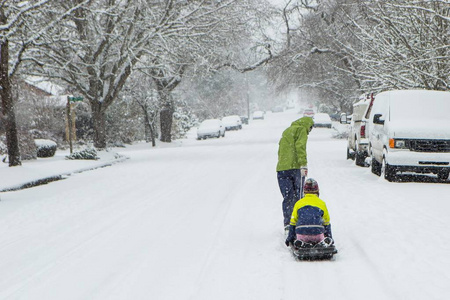 孩子们沿着一条空荡荡的街道的中心走着，拖着雪橇在刚刚落下的冬季雪中行驶。