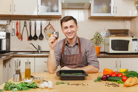 穿着围裙坐在餐桌上的帅气的年轻人, 在家里做饭, 准备猪肉,牛肉或